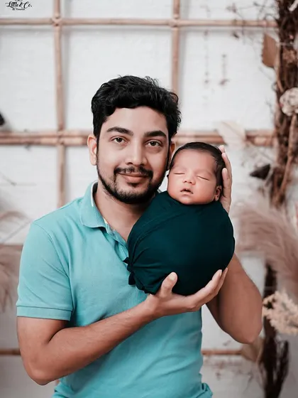 A proud father holds his swaddled newborn, smiling at the camera. This portrait captures the joy and wonder of new fatherhood in our beautifully lit studio.