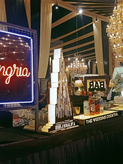 A stylish Sangria station with a neon sign, set up as part of a larger bar for a wedding reception.