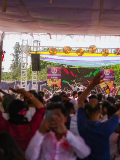 A view from the back of the crowd at a massive Holi party. The energy is contagious, with everyone's hands in the air.