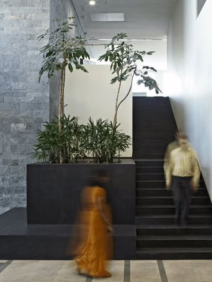 The lobby of the KMC Headquarters features clean lines, natural materials like slate, and integrated planters. The motion-blurred figures suggest the flow of people through this calm and ordered transitional space.