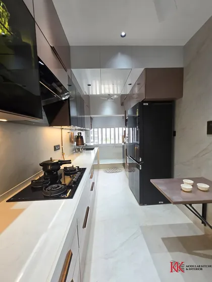 This parallel modular kitchen at Kalpataru Heights features a back-painted glass finish and premium Häfele hardware. The layout includes a tall unit, rolling shutter, and ample drawer space for a clutter-free experience.