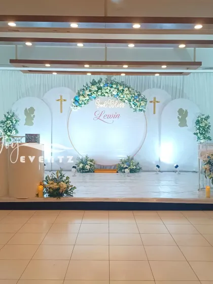 This is a complete stage decoration we did for a baptism ceremony. The design features a large central ring, elegant white drapes, and beautiful blue and white floral arrangements, transforming the entire venue.