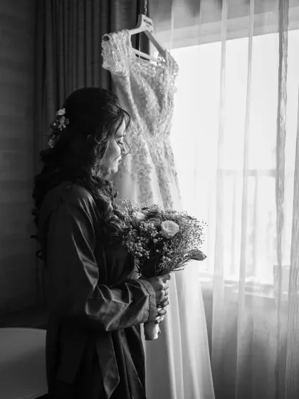 A beautiful black and white shot of the bride with her dress hanging in the background. This artistic photo captures a quiet moment of anticipation.
