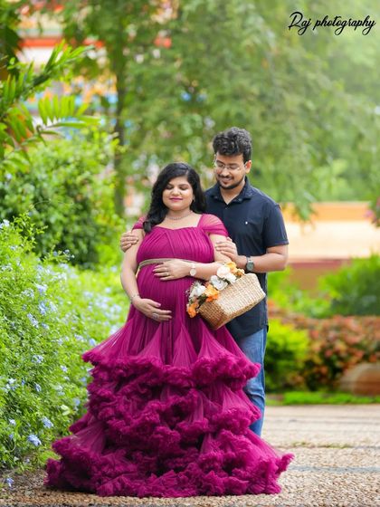 A lovely couple's portrait in a garden, with the mother-to-be holding a basket of flowers and wearing a wine-colored ruffled gown.