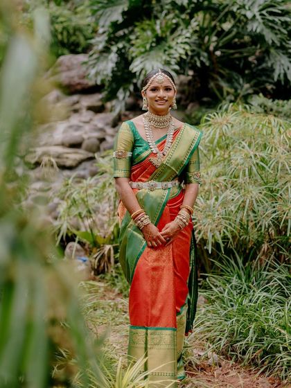 A full-length shot of the bride in the lush green landscape of Coorg. The vibrant colors of her saree and the intricacy of her temple jewelry are the focus, supported by classic, elegant makeup.