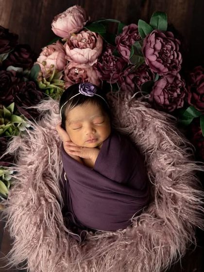 This angle shows the baby surrounded by a wreath of deep purple and pink flowers, creating a lovely frame for their sleeping face.