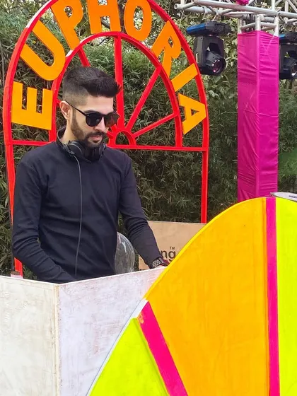 Behind the decks at a vibrant outdoor Mehendi ceremony with a 'Euphoria' theme. Daytime events require a different musical approach, often involving more melodic and upbeat tracks to match the sunny atmosphere.