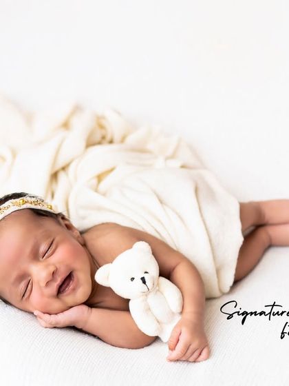 A happy, smiling newborn dreaming sweet dreams, holding a tiny teddy bear.