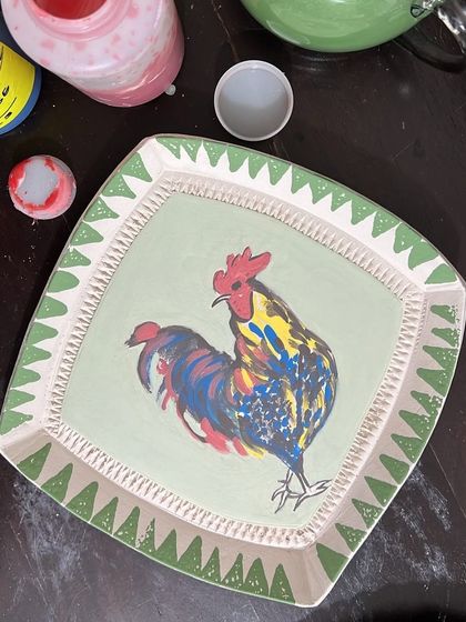 A work-in-progress shot of a folksy rooster plate. I'm using underglazes to hand-paint the design, layering colors to create a vibrant, illustrative piece of stoneware.