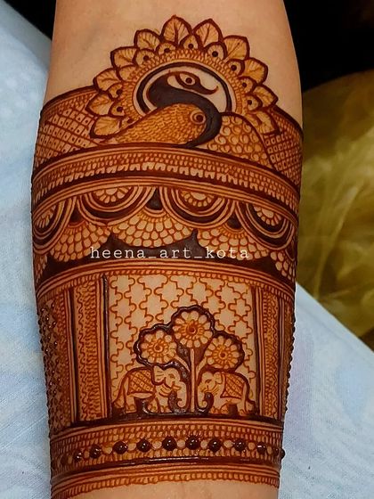 A detailed close-up of an armband design. It features a peacock in the sun and elephants under a tree, showcasing our skill in creating miniature scenes with henna.