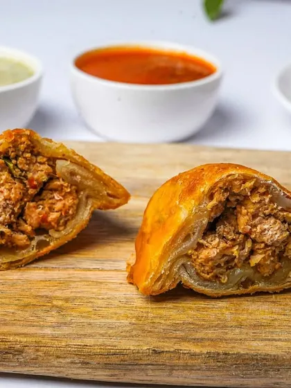 A close-up of a chicken samosa, split open to display the savory minced chicken filling. The clean background and sharp focus make this an effective and appetizing menu photo.