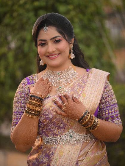 A smiling bride in her purple and gold saree. The rich colors and intricate details make this a truly memorable bridal outfit.