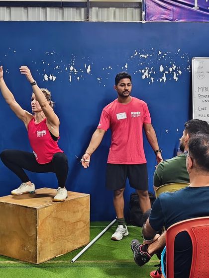 A practical demonstration during a seminar, with a coach teaching proper squat form on a box to the class.
