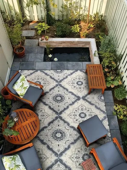 Even a compact backyard can become a personal oasis. This design utilizes vertical space with climbing plants and a raised pond with water lilies. The seating area, defined by an outdoor rug, creates a cozy and inviting corner for relaxation.