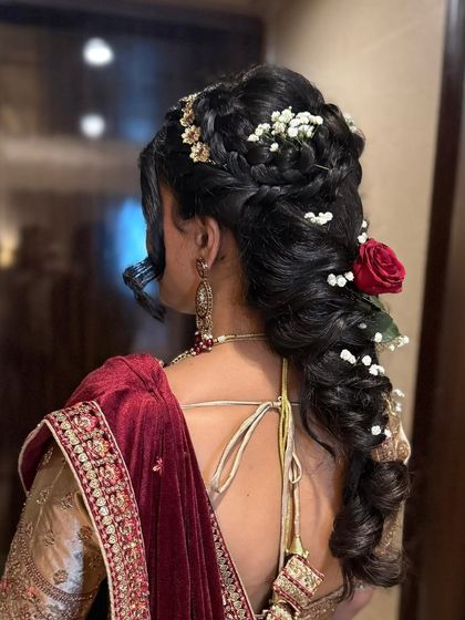 A detailed look at an intricate bridal hairstyle from the back. This style combines braids, curls, and floral accessories, creating a stunning and secure updo perfect for supporting a dupatta and lasting through the entire celebration.