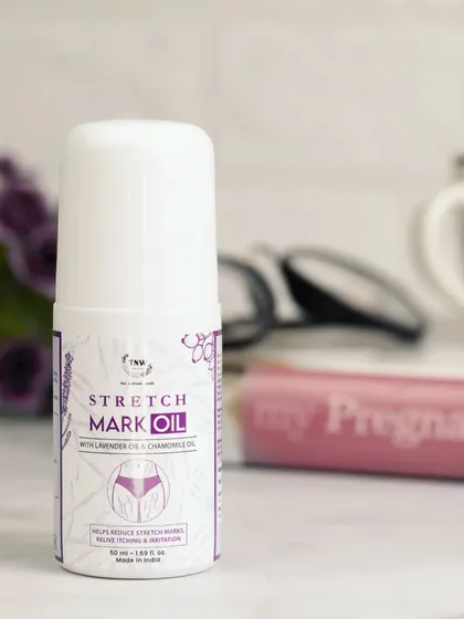 This lifestyle shot places the stretch mark oil on a desk next to a pregnancy book. This thoughtful context directly speaks to the intended audience and highlights the product's specific purpose.