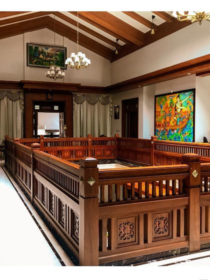 Another view of the traditional Kerala home's interior, highlighting the rich texture of the wooden ceiling and railings. The space is decorated with traditional art, completing the heritage-inspired aesthetic.