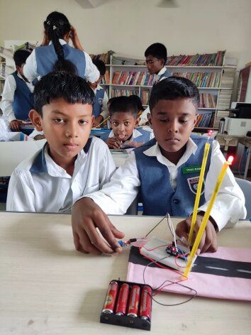 Young students proudly work on their smart street light project, connecting batteries and checking the LED indicators.