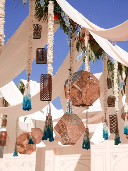 A ceiling decorated with flowing drapes, geometric copper lanterns, and blue tassels. This design created a beautiful, shaded canopy for a sunny outdoor event.