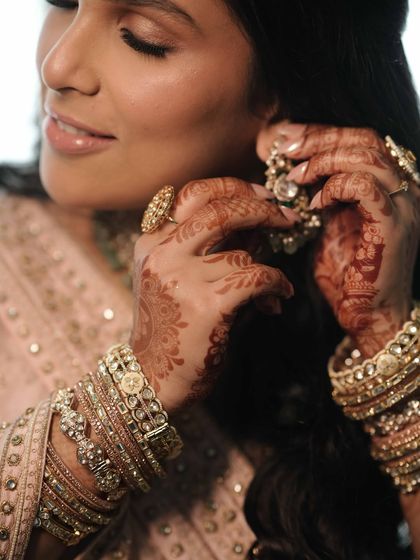 Details of a pastel pink bridal look. The soft golden hues on the eyes and glowing skin are complemented by the intricate henna and beautiful bangles.