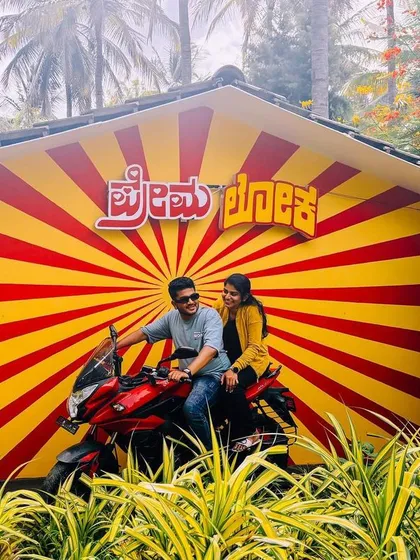 A fun and candid shot of a couple on a motorcycle in front of our 'Premaloka' movie backdrop.