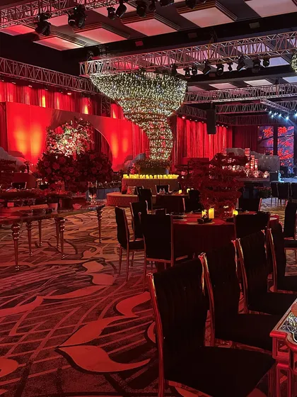 A wide view of the red-themed Sangeet, showing the central floral tornado, velvet-draped tables, and dramatic red lighting that enveloped the entire ballroom.