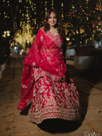 A stunning night-time bridal portrait. The bride's red lehenga glows against the background of fairy lights.