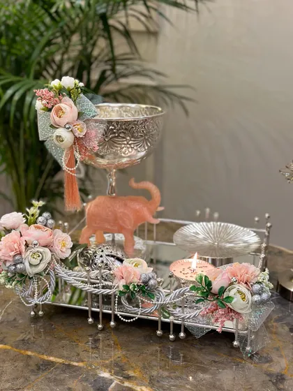 A luxurious Diwali hamper featuring a silver mirror tray, an ornate silver bowl, and a cute pink elephant figurine. The soft pink and silver color scheme creates a modern yet traditional aesthetic.