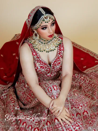 A full view of a modern bride in a traditional red lehenga. The makeup is balanced to complement the heavy embroidery and jewelry, ensuring the bride's natural beauty remains the centerpiece.