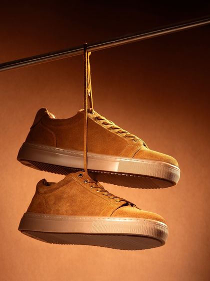 A creative shot of hanging suede sneakers with a drip of honey, creating a unique visual that plays on the shoe's "honey" color.