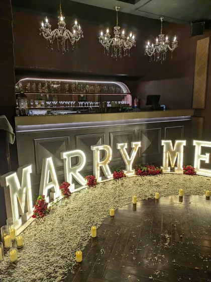 The full proposal decoration viewed from the side, highlighting the scale of the marquee letters against the backdrop of the venue's bar and chandeliers.