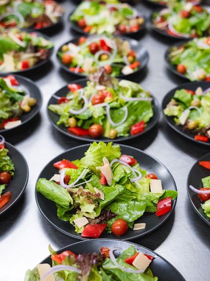 Rows of fresh salads being prepped for a large event. We ensure every dish, big or small, is made with care and consistency.