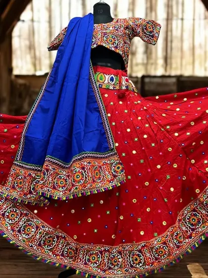 A classic red chaniya choli with intricate multi-color embroidery and mirror work along the border. The contrasting royal blue dupatta makes the entire outfit pop.