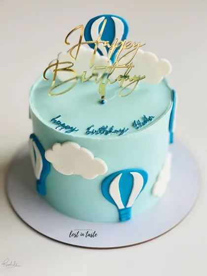 A whimsical hot air balloon themed cake. The light blue buttercream sky, fluffy clouds, and a golden "Happy Birthday" topper make it a delightful choice for a child's celebration.