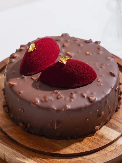 Our Belgian Chocolate and Hazelnut Fudge cake, cloaked in a glossy rocher glaze and topped with delicate red velvet accents. This is a masterpiece of fudgy, crunchy, can’t-stop magic.