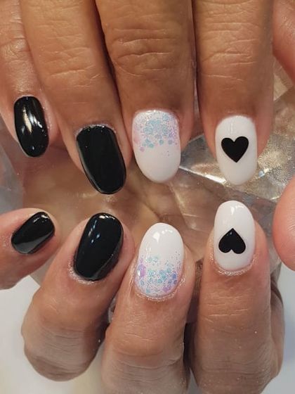 A trendy and chic black and white nail design. This set plays with contrasts, featuring solid black nails, a glittery white accent nail, and a white nail with a simple black heart sticker.