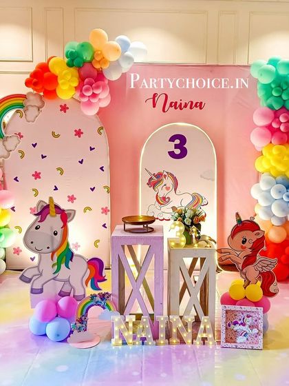 A bright and colorful rainbow unicorn party. This setup features a unique backdrop, rainbow-colored balloon columns, cute unicorn cutouts, and a rainbow-striped floor mat.