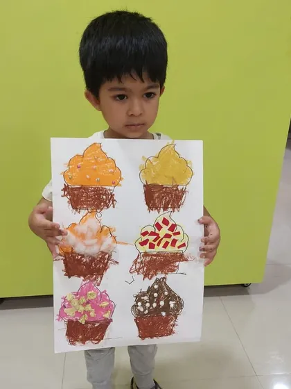 A proud student showing off his finished cupcake collage. He used cotton balls, paper, and other materials to create different "frosting" textures on each cupcake.