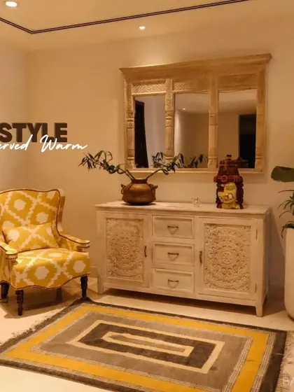 Style served warm. This cozy corner features intricately carved wooden furniture, a patterned yellow armchair, and a matching rug to create a warm and inviting atmosphere.
