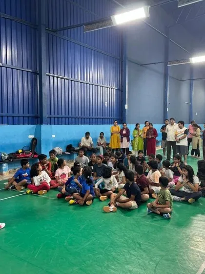 Learning is a group activity. A coach addresses our summer camp students, explaining game strategy and techniques before a practice session, with parents watching from the sidelines.