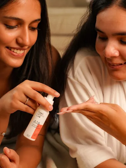 A candid shot of two women enjoying a skincare product together. The natural smiles and shared experience make the brand feel approachable and perfect for a relaxing self-care routine with friends.