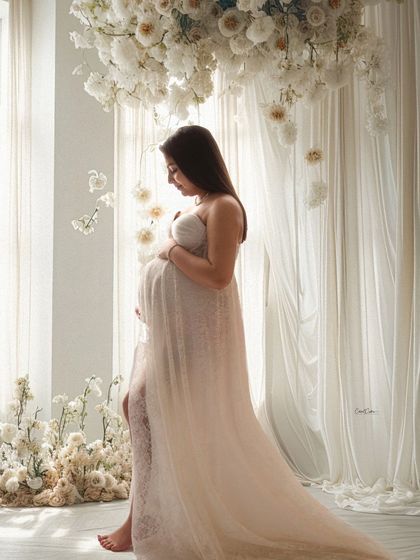 A soft, dreamy profile shot by the window. The light filters beautifully through the sheer curtains and the mom-to-be's white gown.