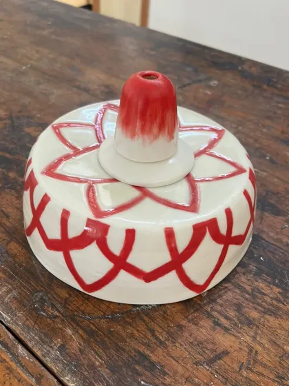 The lampshade after the first firing and painting, but before the gold lustre is added. The red color is vibrant and glossy.