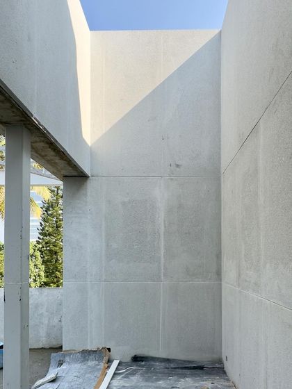A light-well under construction, with the sun creating a sharp diagonal line on a raw concrete wall.