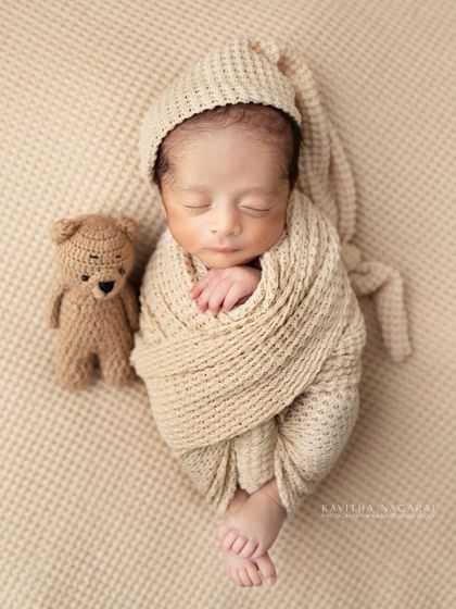 A newborn wrapped in a neutral-toned swaddle, resting next to a tiny crocheted teddy bear. The simple props add a touch of sweetness without distracting from the baby.
