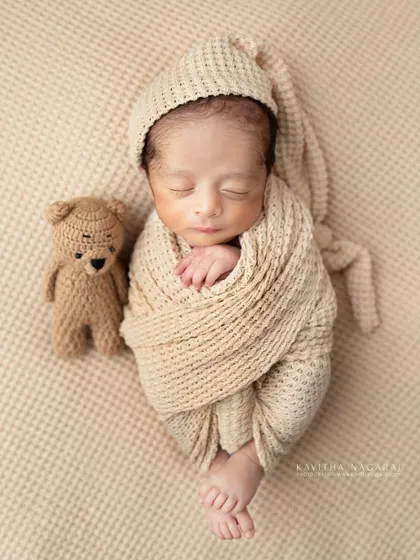 A newborn wrapped in a neutral-toned swaddle, resting next to a tiny crocheted teddy bear. The simple props add a touch of sweetness without distracting from the baby.