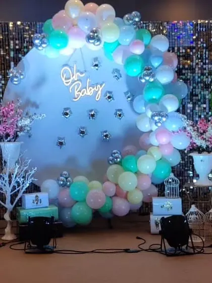 An elegant baby shower setup with a shimmering sequin backdrop, a circular frame with pastel balloons, and a neon "Oh Baby" sign.