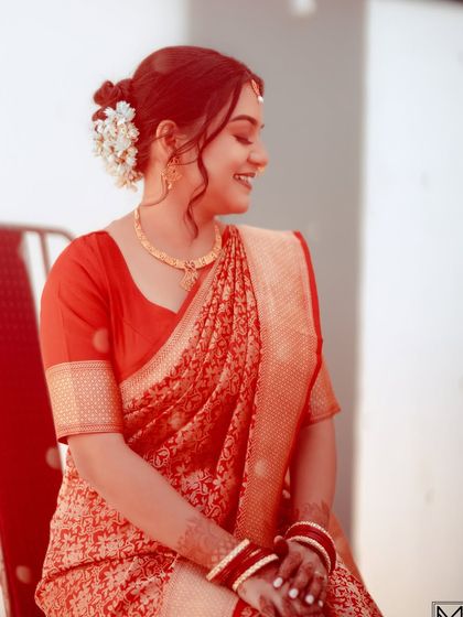 A simple, elegant portrait of a bride in a red saree, her hair in a classic bun with flowers.