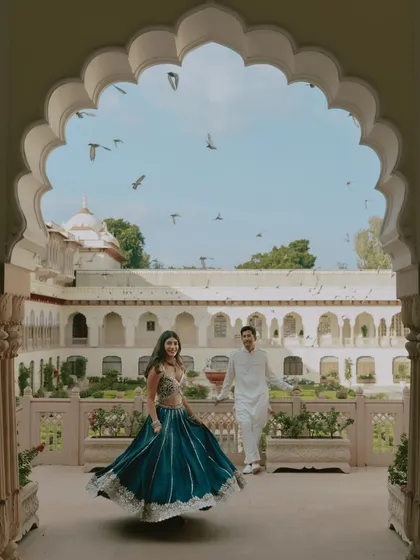 A joyful, unscripted moment at Rambagh Palace. Framed by a classic Rajasthani archway, she twirls in her vibrant lehenga as birds take flight, capturing the spontaneous energy and heritage of a royal pre-wedding shoot in Jaipur.