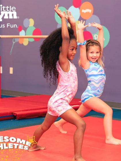 Two young gymnasts strike a pose, practicing their balance and form. Our classes teach children to work together and learn from each other, building both skills and friendships.